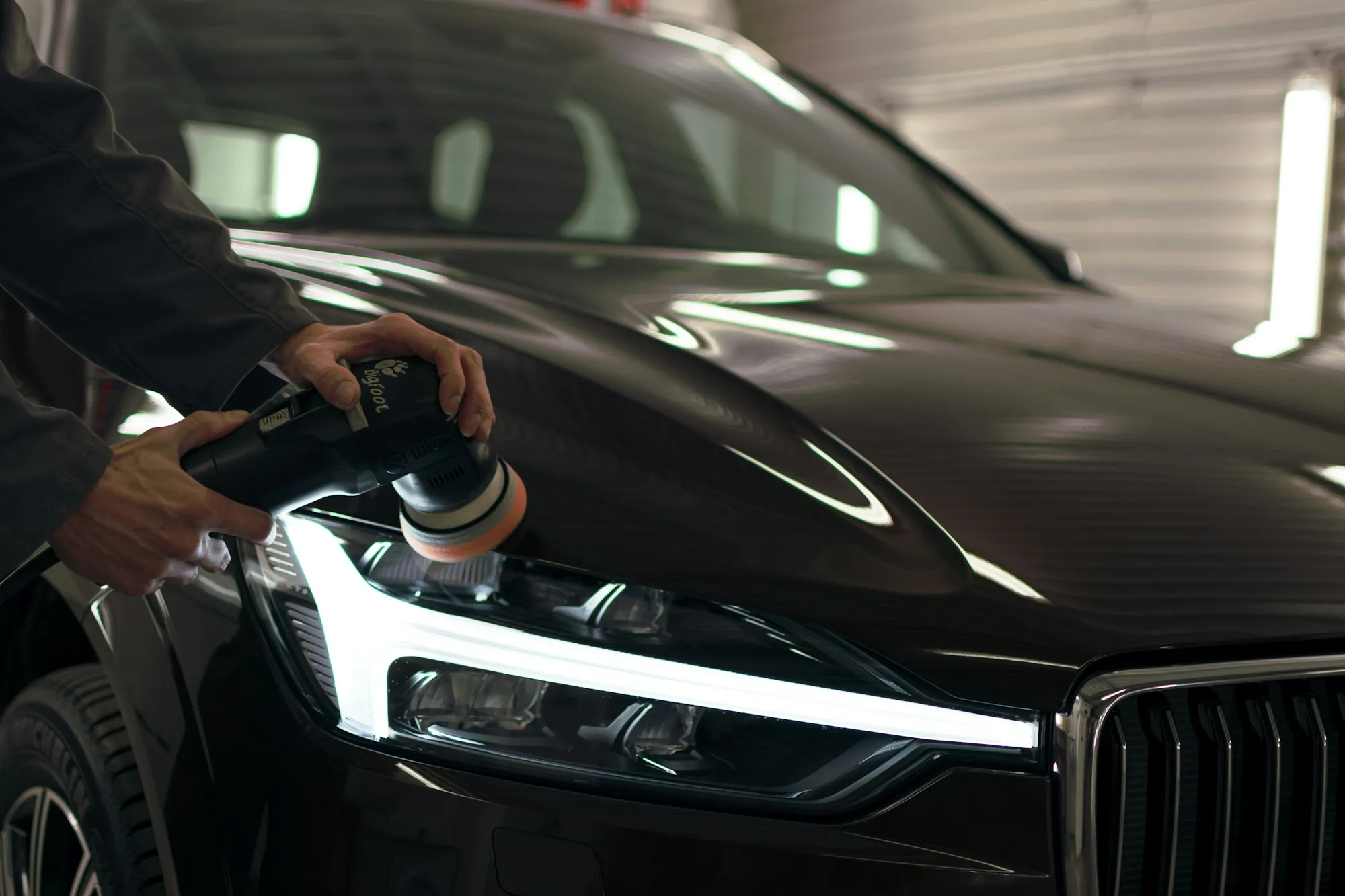 Technician polishing the headlight of a dark SUV